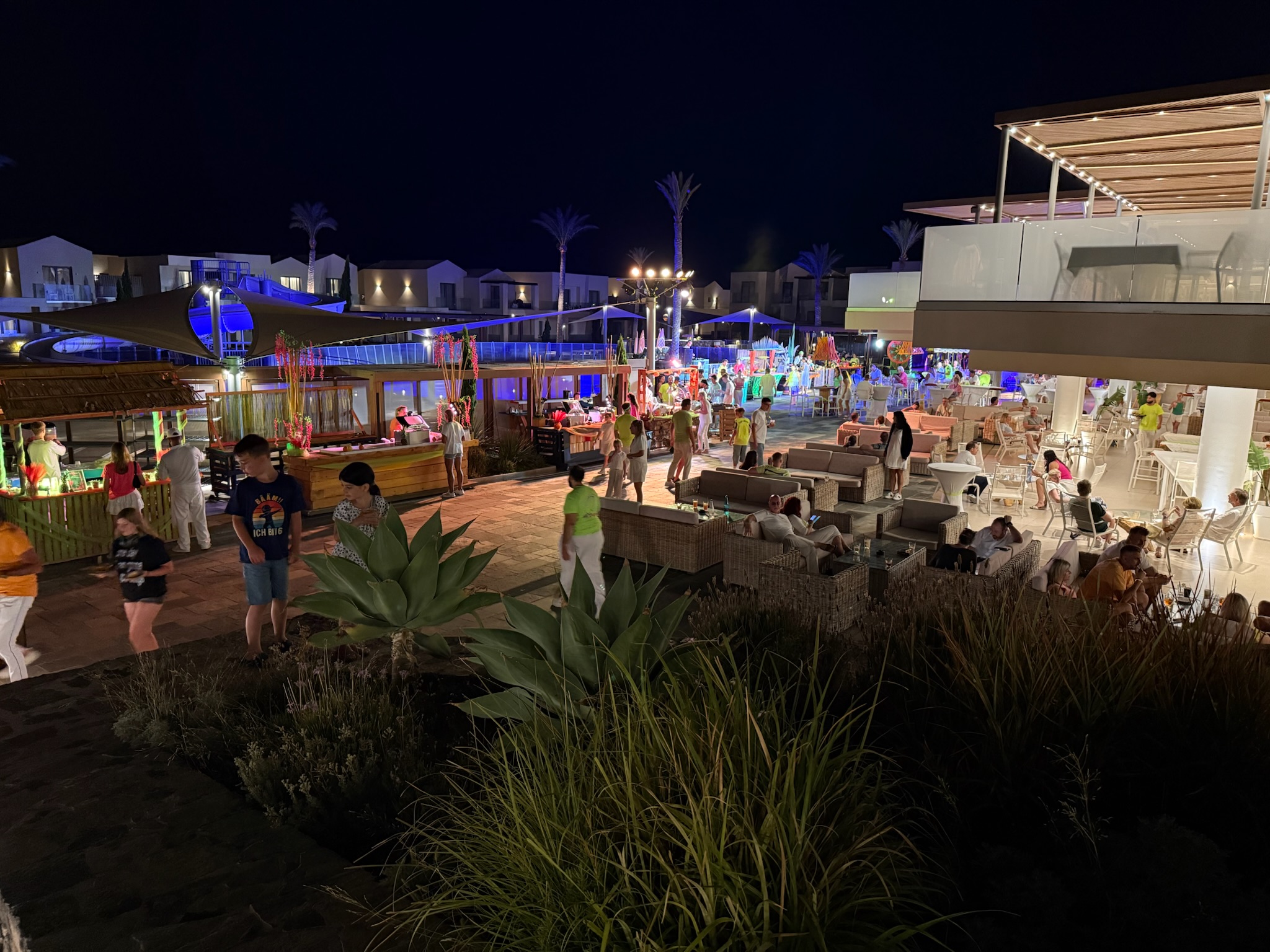 Beleuchteter Außenbereich des ROBINSON Ierapetra mit Gästen, Bars und Sitzgruppen.